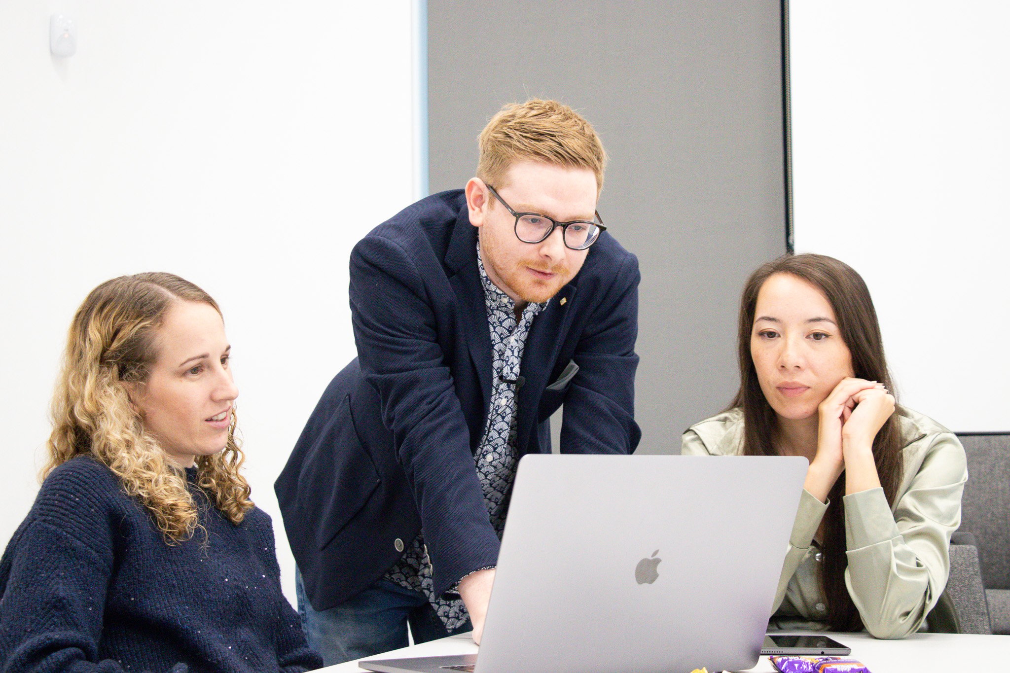 Tom Wardman leaning over a laptop with two members of a client’s marketing team, working through the plan together in their meeting room.