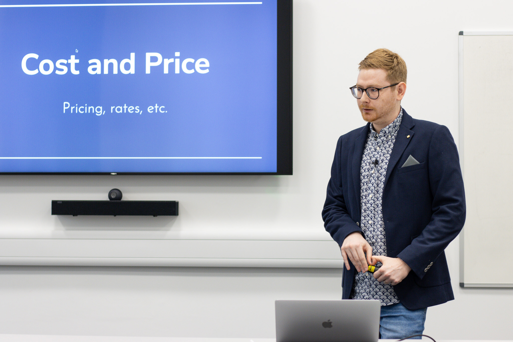 Tom Wardman presenting a session on cost and price, with the slide “Cost and Price” on the screen behind him.