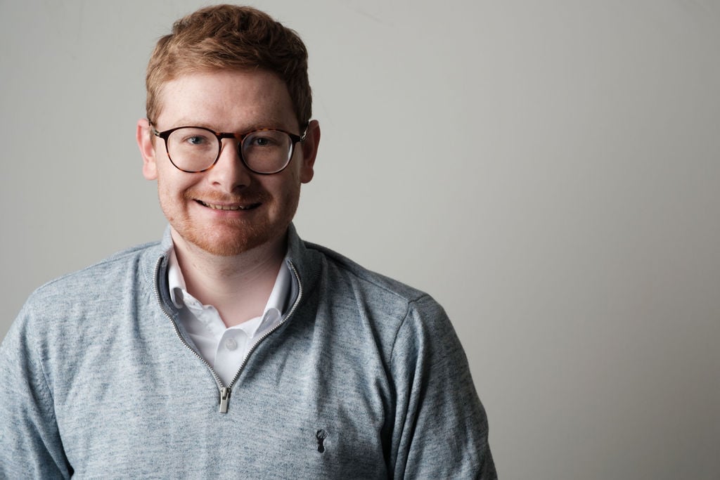 Tom Wardman smiling at the camera in a grey quarter-zip jumper.