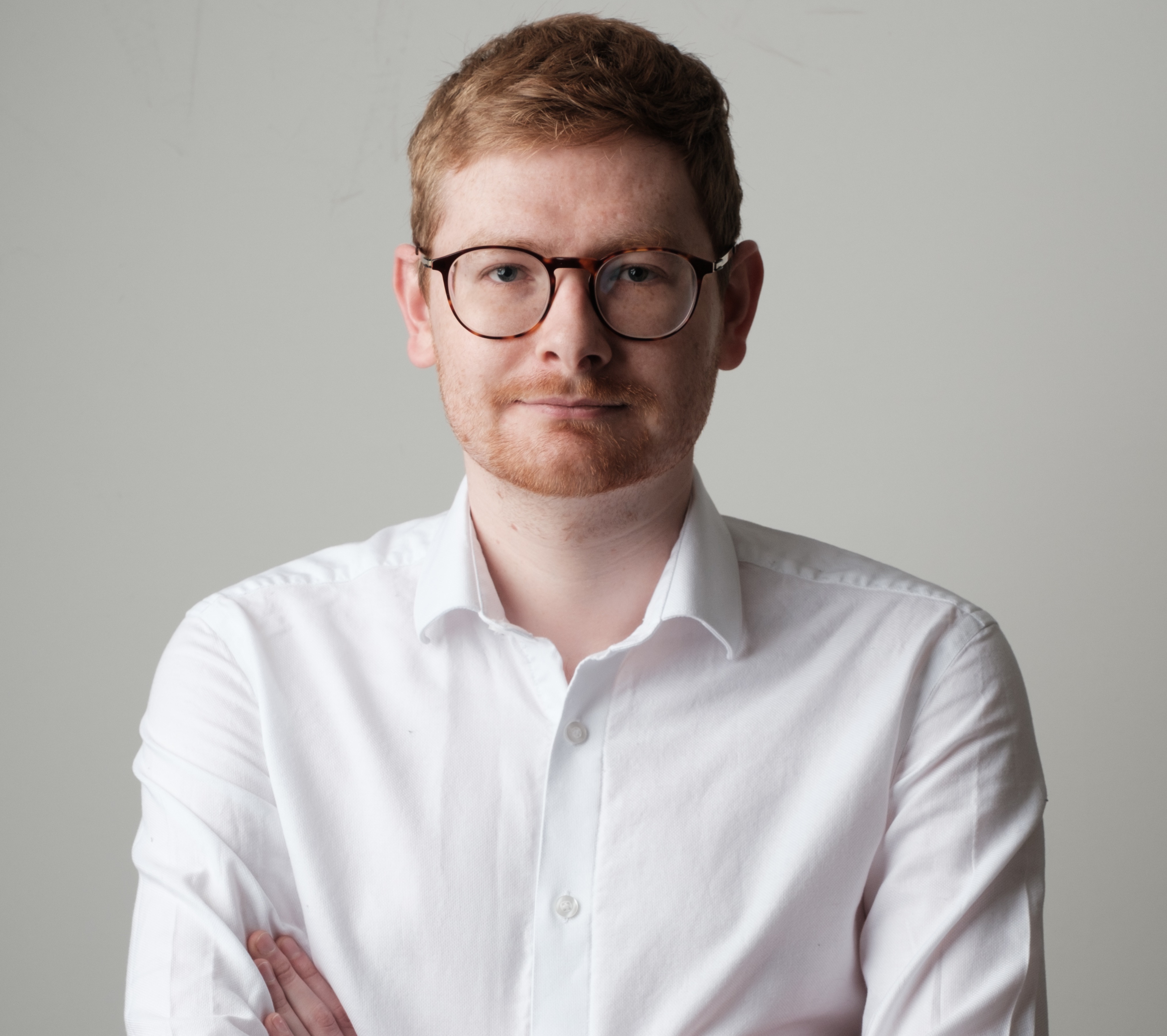 Tom Wardman, facing the camera with arms folded and open neck white shirt.