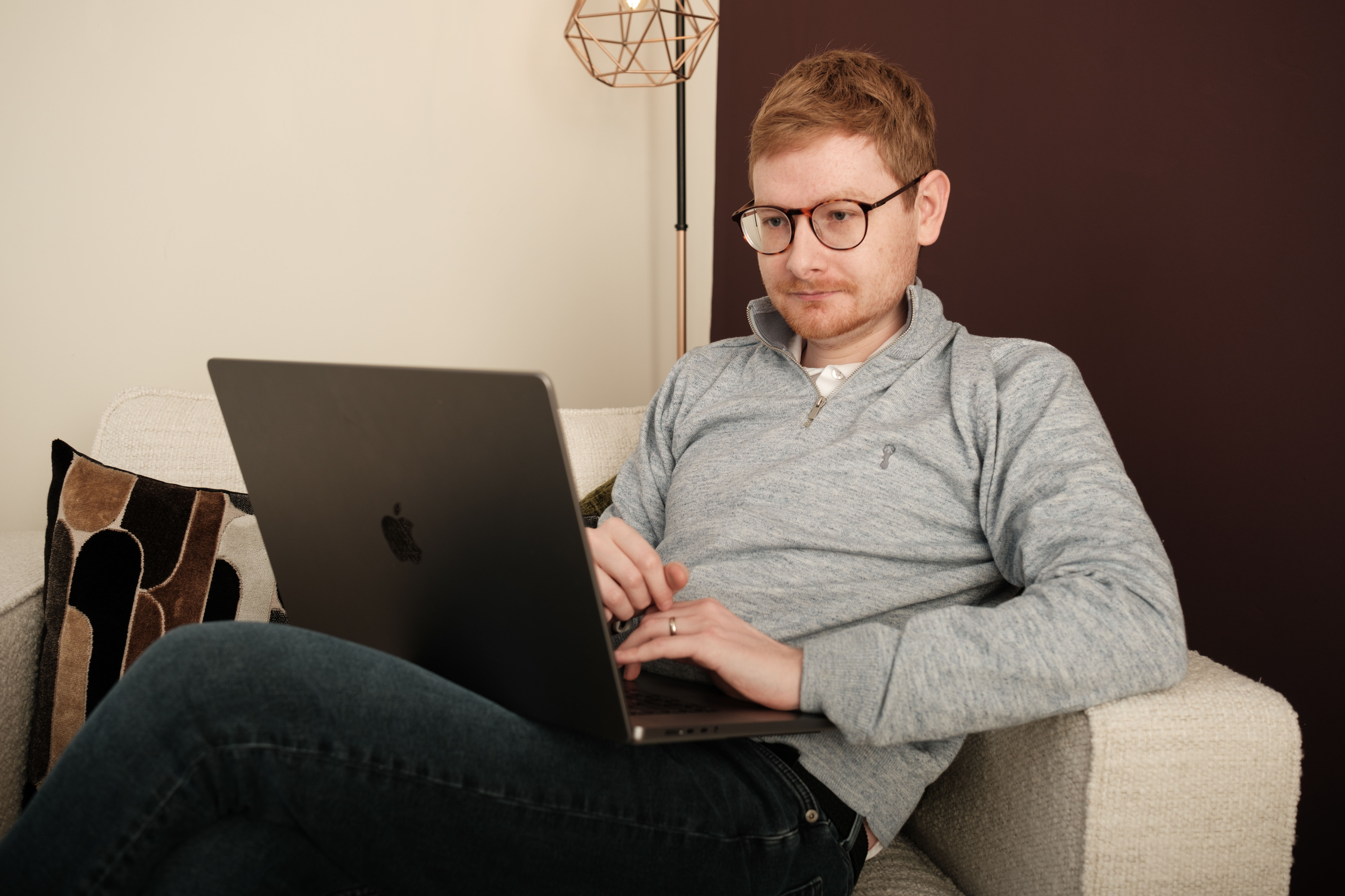 Tom Wardman relaxing on a sofa with a laptop, smiling at the camera.