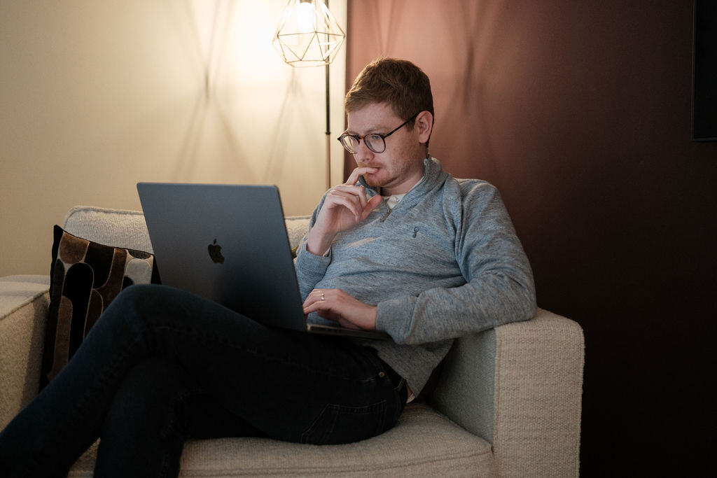 Tom Wardman sitting back on a sofa with a laptop, relaxed as he reviews a client’s work.