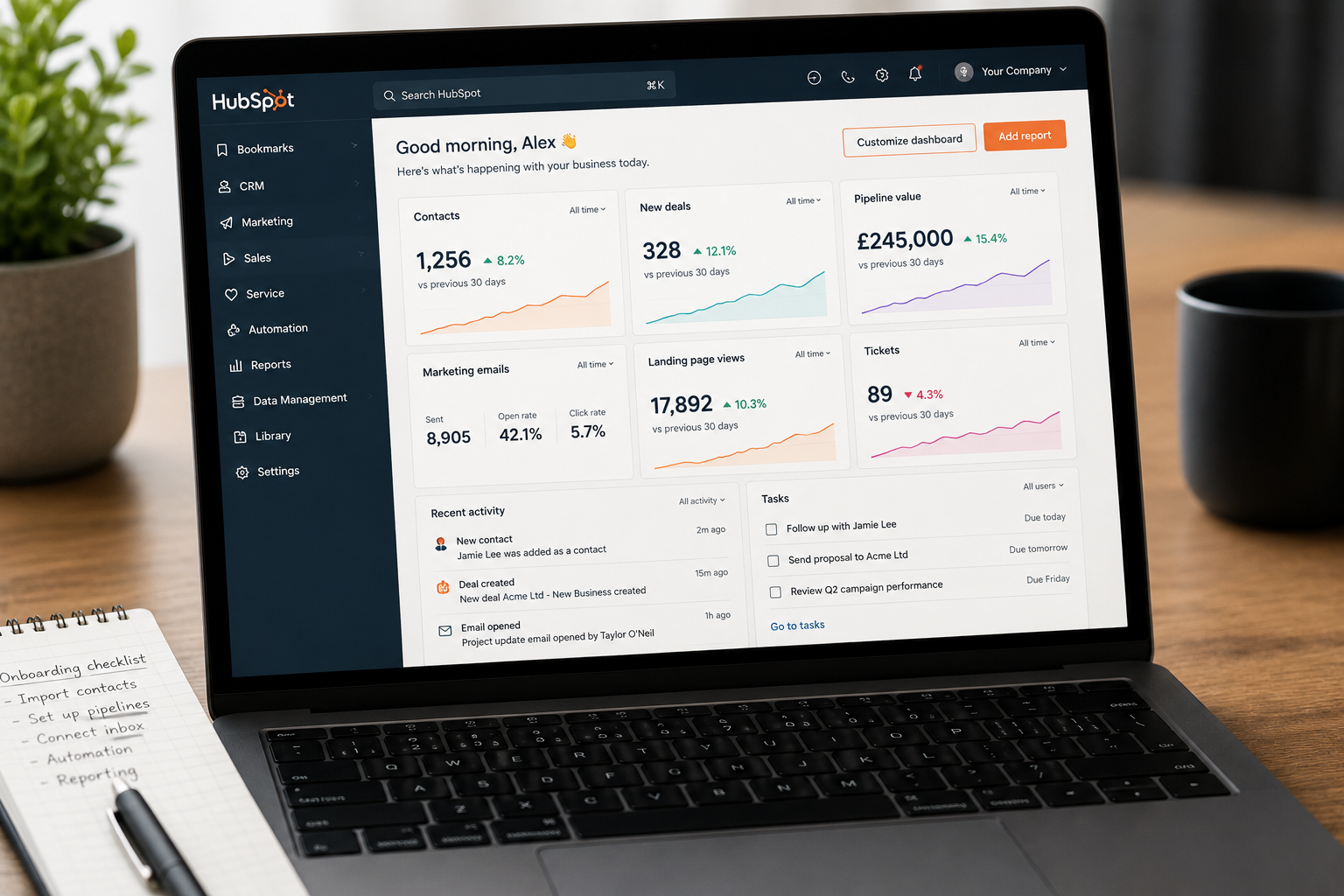HubSpot portal open on a laptop during initial onboarding configuration. The dashboard displays contacts, deals, pipeline value, marketing performance, tasks, and reporting widgets, while an onboarding checklist on the desk highlights activities such as importing contacts, configuring pipelines, connecting email, setting up automation, and validating reports. The image represents the early stages of a structured HubSpot implementation and portal setup.